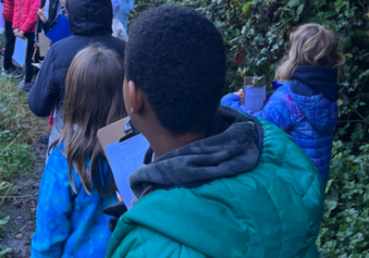 Elementary school students walking along Longfellow Creek in West Seattle, recording day, time, temperature, and precipitation to learn about water moments.