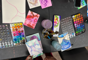 A vibrant tabletop filled with watercolor palettes, brushes, and colorful artwork in progress, showcasing the creativity and expression of participants during an art session.