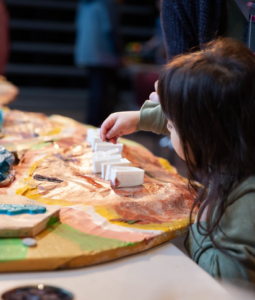 A child sprinkles sand around block letters spelling “Delridge” on a 3D map of Longfellow Creek.